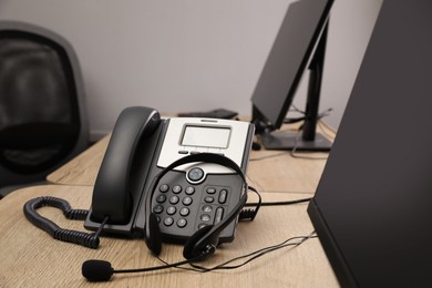 Stationary phone and headset on wooden desk in office. Hotline service