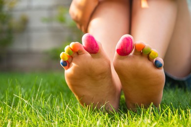 Teenage girl with painted toes sitting on green grass outdoors, closeup