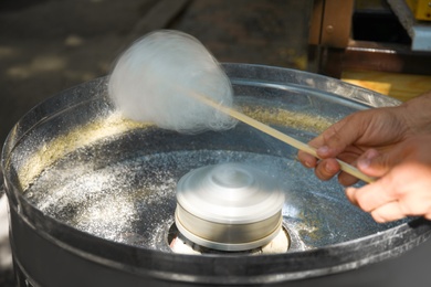 Photo of Man making cotton candy using modern machine outdoors, closeup