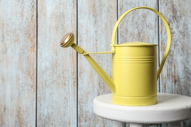 Yellow metal watering can on white table against wooden background