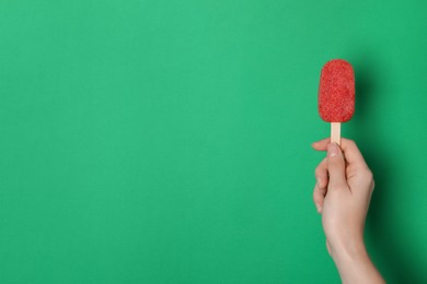 Woman holding tasty fruit ice pop on green background, space for text