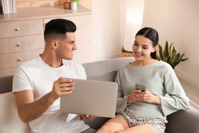 Photo of Happy couple in pyjamas with gadgets spending time together on sofa at home