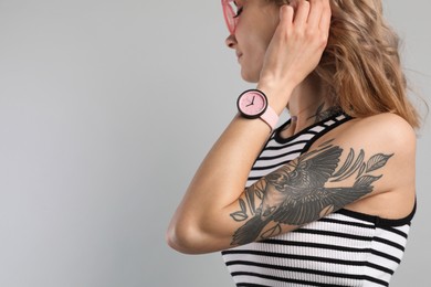 Beautiful woman with tattoos on arm against grey background, closeup. Space for text