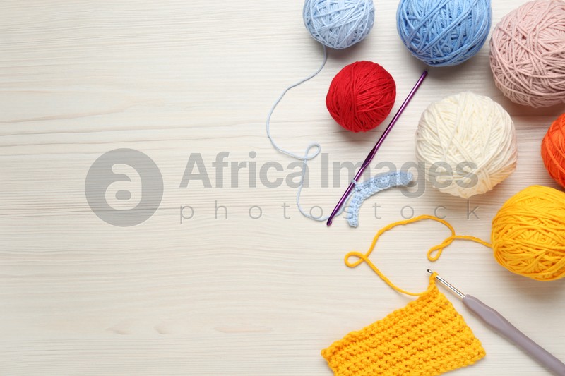 Flat lay composition with knitting threads and crochet hooks on white wooden table, space for text
