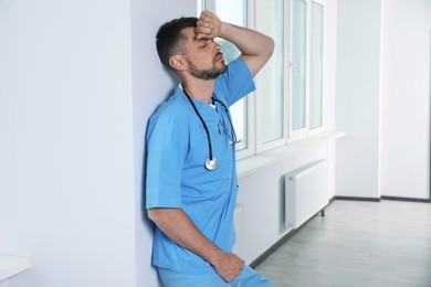 Exhausted doctor near white wall in hospital hallway