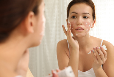 Teen girl with acne problem applying cream near mirror in bathroom