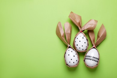 Photo of Easter bunnies made of craft paper and eggs on light green background, flat lay. Space for text