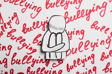 Child paper figure and words Bullying written on white background, top view