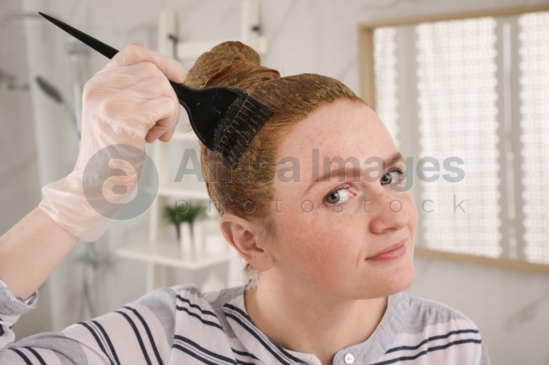 Young woman dyeing her hair with henna in bathroom