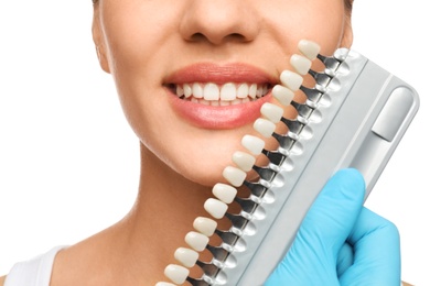 Doctor checking young woman's teeth color on white background, closeup. Cosmetic dentistry