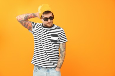 Photo of Handsome hipster man wearing stylish sunglasses on orange background. Space for text
