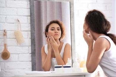 Beautiful young woman with acne problem looking in mirror at home