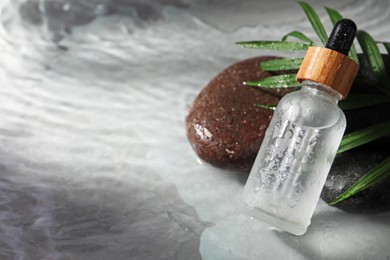 Bottle of face serum, spa stones and leaf on wet grey marble table, closeup. Space for text