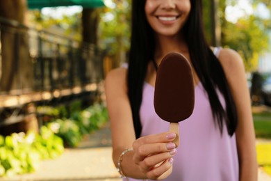Young woman holding ice cream glazed in chocolate on city street, closeup. Space for text