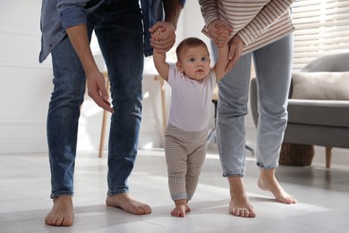 Photo of Parents supporting their baby daughter while she learning to walk at home