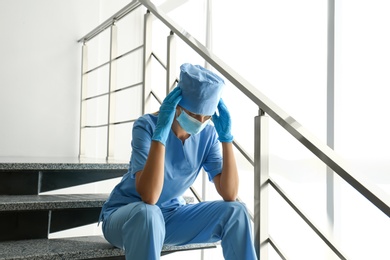 Exhausted doctor sitting on stairs in hospital. Stress of health care workers during COVID-19 pandemic