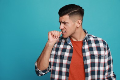 Man biting his nails on light blue background, space for text. Bad habit