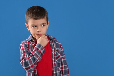 Thoughtful little boy on blue background, space for text