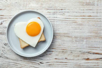 Photo of Romantic breakfast with heart shaped fried egg and toast on white wooden table, top view. Space for text