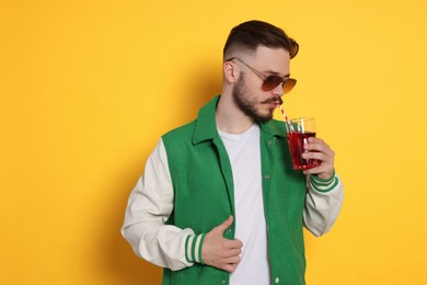 Photo of Handsome young man drinking juice on yellow background
