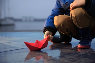 Little boy playing with paper boat near puddle on pier, closeup