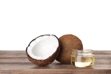 Coconuts and jar of natural organic oil on wooden table against white background