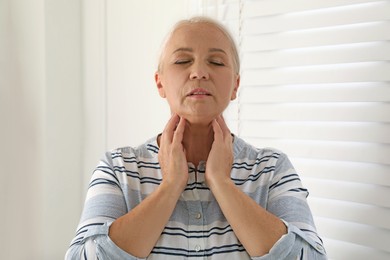Mature woman doing thyroid self examination indoors