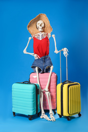 Human skeleton in summer clothes with suitcases on blue background