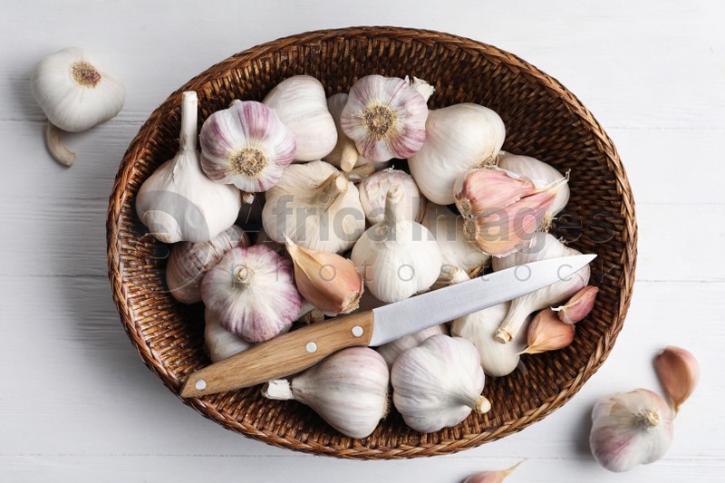 Fresh organic garlic in wicker basket on white wooden table, flat lay