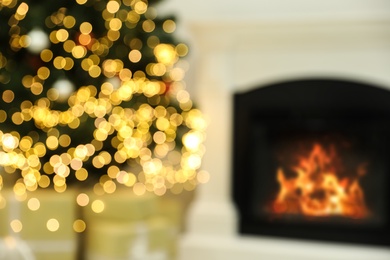 Blurred view of Christmas tree with bright string lights in room near fireplace. Bokeh effect