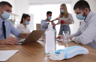 Protective masks, hand sanitizer and blurred view of coworkers on background. Business meeting during COVID-19 pandemic