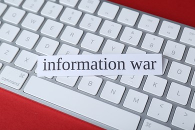 Photo of Paper card with words Information War and keyboard on red background, closeup