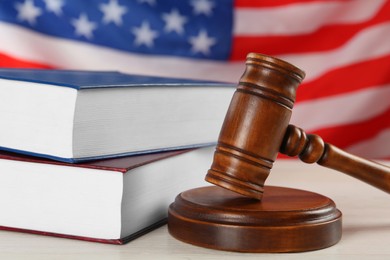 Judge's gavel and books on white wooden table against American flag, closeup