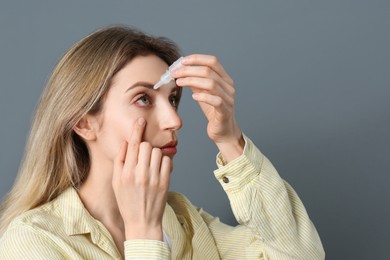 Woman using eye drops on dark grey background