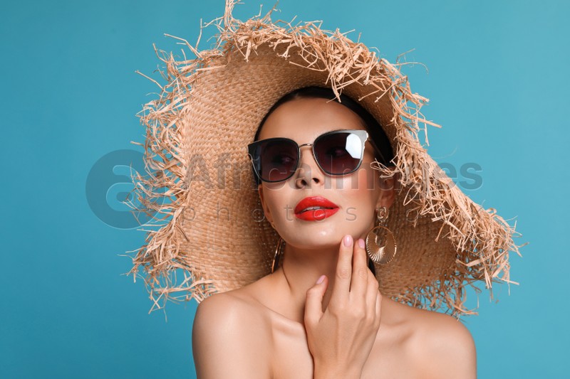 Attractive woman in fashionable sunglasses and wicker hat against light blue background