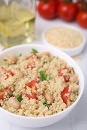 Photo of Delicious quinoa salad with tomatoes, beans and parsley served on white tiled table, closeup