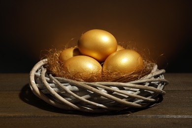 Shiny golden eggs in nest on wooden table