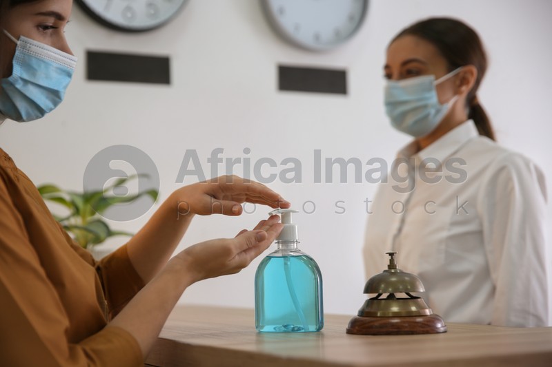 Photo of Woman applying antiseptic gel at hotel reception, closeup