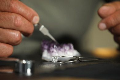 Professional jeweler working with beautiful amethyst at table, focus on tweezers