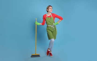 Young housewife with broom on light blue background