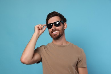 Portrait of smiling bearded man with stylish sunglasses on light blue background