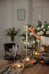 Woman lightning up candle at dining table indoors, closeup. Festive setting