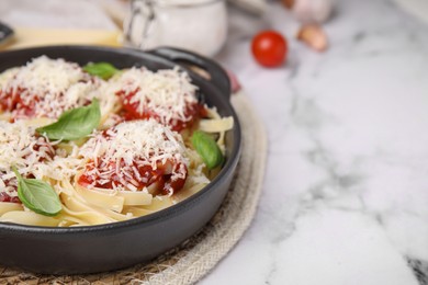 Delicious pasta with tomato sauce, basil and parmesan cheese on white marble table, closeup. Space for text