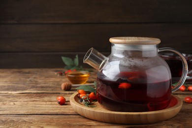 Teapot with aromatic rose hip tea and fresh berries on wooden table, space for text