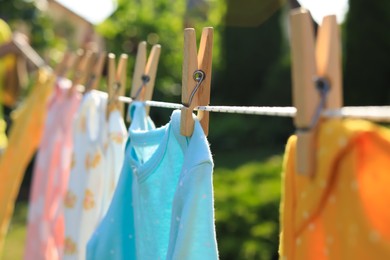Clean baby onesies hanging on washing line in garden, closeup. Drying clothes