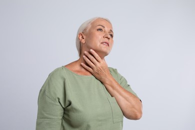 Mature woman doing thyroid self examination on light grey background