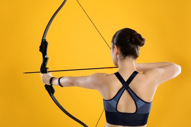 Woman with bow and arrow practicing archery on yellow background, back view