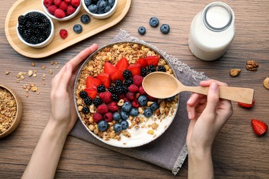 Photo of Woman eating healthy muesli served with berries at wooden table, top view