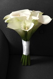 Photo of Beautiful calla lily flowers tied with ribbon on sofa