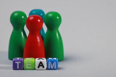Colorful pawns and cubes with word Team on light grey background, closeup with space for text. Recruiter searching employee
